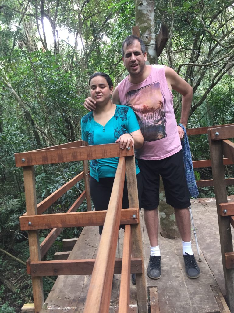 Atena e Marlon em pé na casinha da árvore com árvores e folhagens